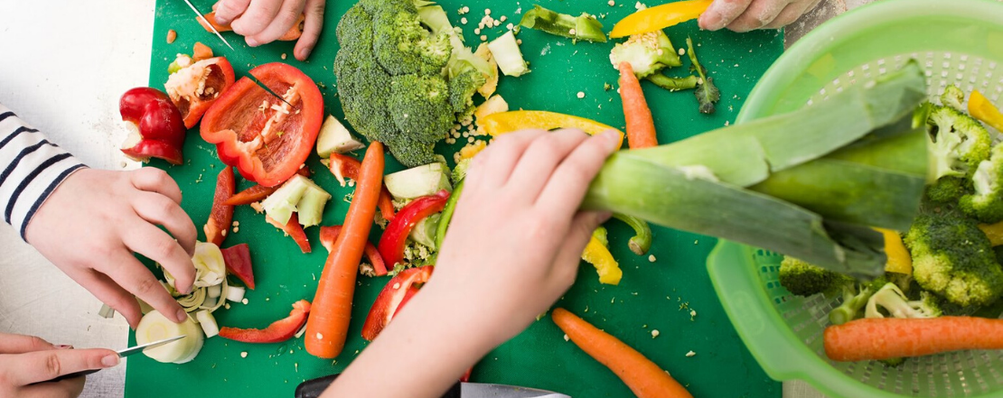 Children's hand chopping vegetables on a green chopping board
