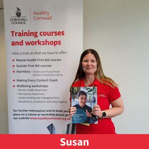 picture of Susan Care, a member of the training team at healthy cornwall, stood next to a training banner, holding a training booklet and smiling