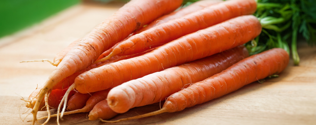 Fresh carrots with green tops on wooden chopping board