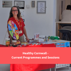 healthy cornwall staff member smiling behind a desk full of stop smoking resources, text reads "Healthy Cornwall - Current programmes"