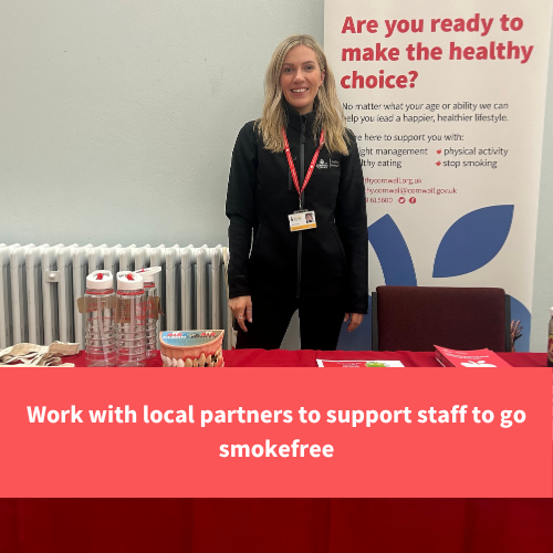 healthy cornwall staff member stood with a table of stop smoking resources, text reads "Work with local partners to support staff to go smokefree"