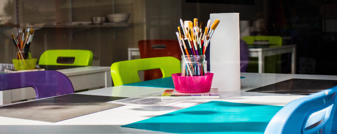 empty desk in classroom with jar of pencil and brushes in the middle of the group of desks