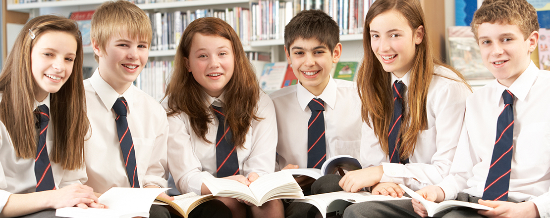 Group of teenagers sat in a library holding open books looking towards the camera